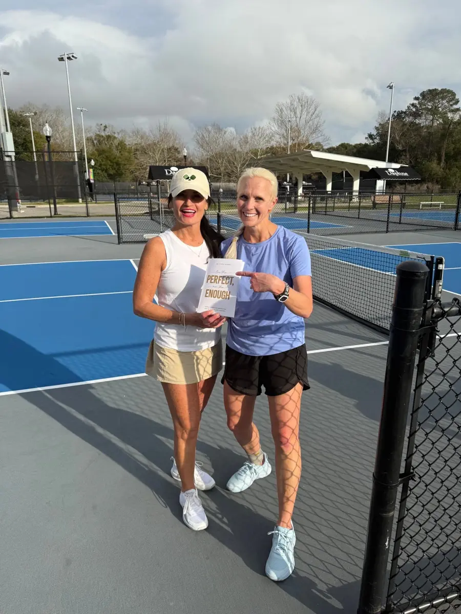 Dr. Sonya Rogers on the pickleball court with a friend holding her book, Less Than Perfect, More Than Enough